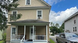 A two-story house with a front porch, a driveway, and a parked truck. - 1st Class Rentals - Munson Manor III at Murdock (Oneonta)