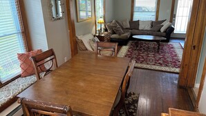 A dining area with a wooden table and chairs, a sofa, and a patterned rug. - 1st Class Rentals - Munson Manor III at Murdock (Oneonta)