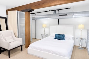 Ett modernt hotellrum med en stor säng, en stol och ett nattduksbord med lampor.