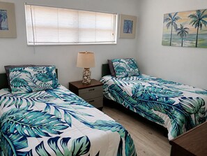 A bedroom with two beds, a nightstand, a lamp, and artwork on the walls.