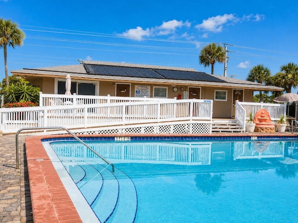 A pool area with a white fence, a lifeguard stand, and a building with solar panels.
