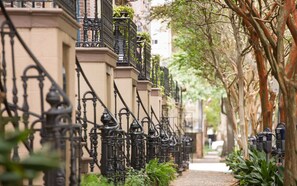 Une rangée de bâtiments agrémentés de balcons en fer forgé noir ouvragé et un chemin bordé d’arbres.