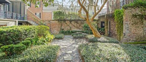 Un patio con sendero de piedra, follaje y una mesa con sillas.
