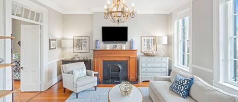 A spacious living room with a fireplace, a chandelier, a television, and a sofa.