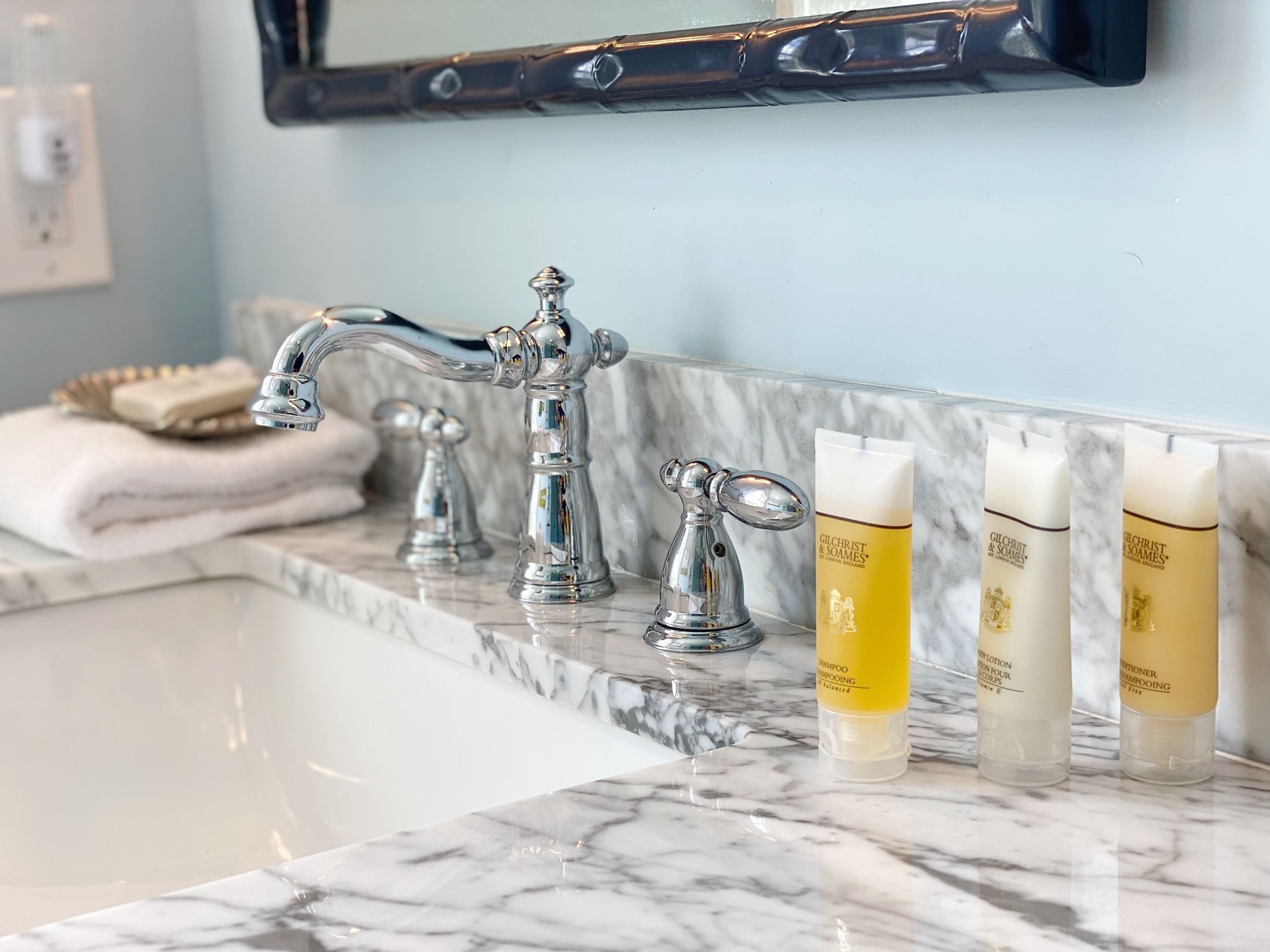 A bathroom with a marble countertop, a chrome faucet, and three Gilchrist & Soames shampoo bottles.