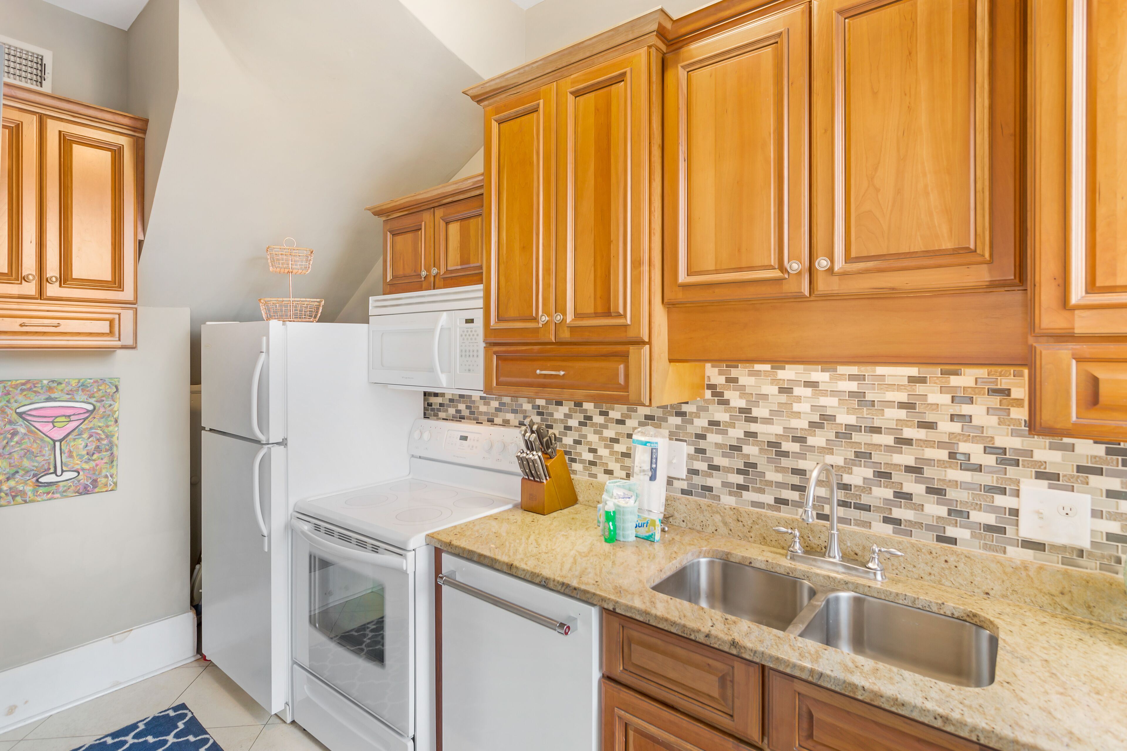 A kitchen with wooden cabinets, a white refrigerator, a microwave, a stove, and a double sink.