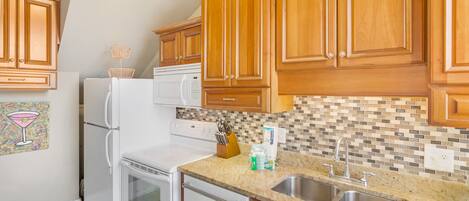 A kitchen with wooden cabinets, a white refrigerator, a microwave, a stove, and a double sink.