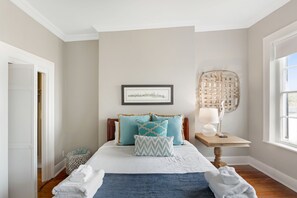 Une chambre à coucher bien rangée, avec un lit, des oreillers, une table de chevet avec une lampe, un tableau encadré au mur et une fenêtre donnant sur un beau paysage.