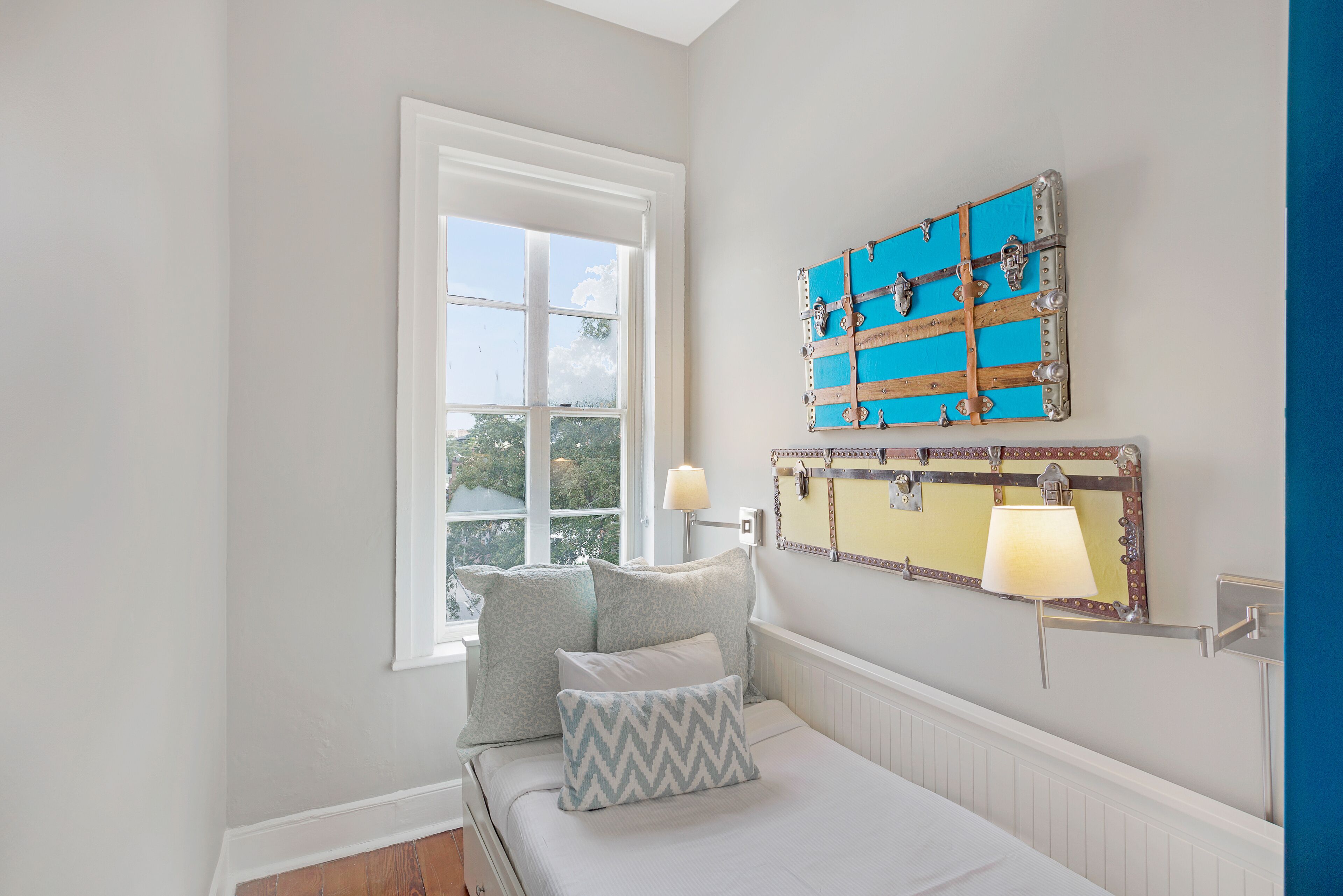 A bedroom with a large window, a bed with pillows, and a wall-mounted lamp.