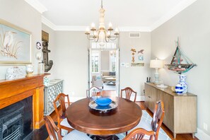 Une salle à manger avec une table en bois, des chaises, un lustre et une cheminée.