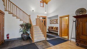 A spacious hallway with a wooden staircase, a large potted plant, a fire extinguisher, and a wooden cabinet.