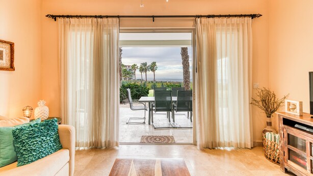 Un salon comprenant un canapé, une table basse et un meuble pour la télévision. Une porte-fenêtre coulissante donne accès à une terrasse extérieure avec une table et des chaises.
