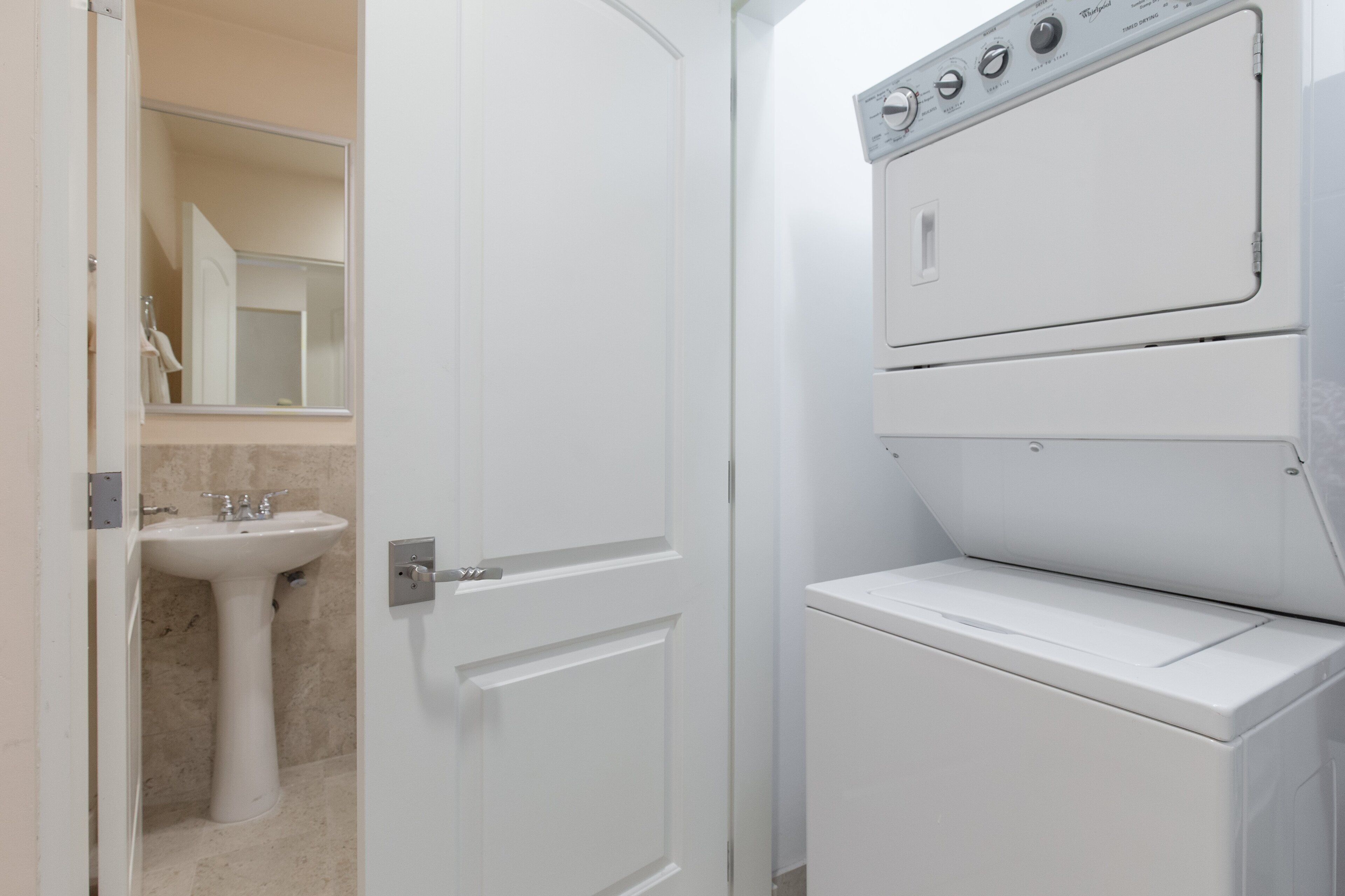A white door leading to a bathroom with a sink and mirror.