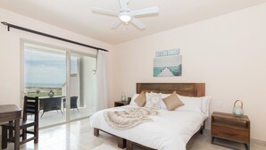 Une chambre dotée d’un grand lit, d’un bureau et d’une chaise, d’un ventilateur de plafond et offrant une vue sur l’extérieur.
