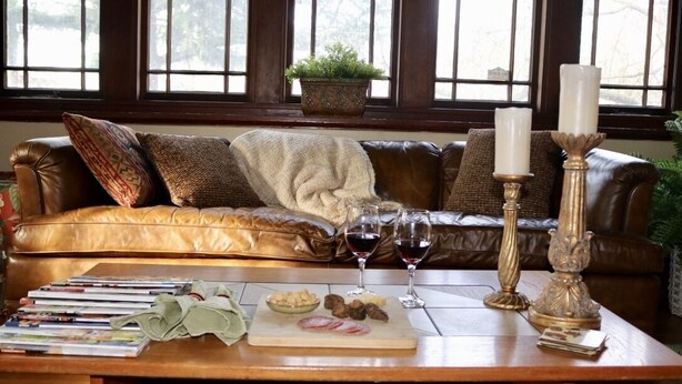 A cozy living room with a leather sofa, a wooden coffee table with magazines, a bowl of snacks, and two wine glasses.