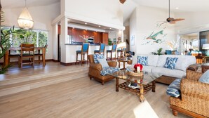 Un grand espace de vie comprenant un canapé, des fauteuils, une table basse et une cuisine en arrière-plan.