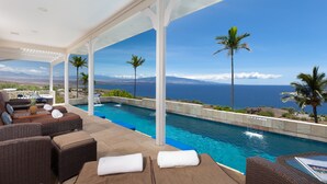 Un espace aménagé au bord de la piscine, avec des meubles en osier, une vue sur l’océan et une cascade décorative.