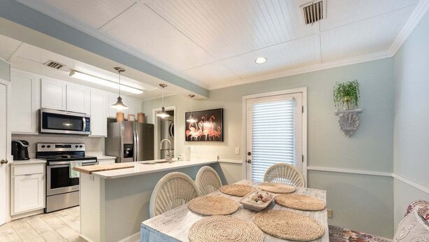 A modern kitchen with white cabinets, stainless steel appliances, and a central island with woven placemats. - Direct Ocean View 2BR Condo Near Pier Village | St. Simons Island Rental (St. Simons Island)