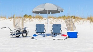 A beach setting with two beach chairs, a beach umbrella, a cooler, and a beach cart. - Direct Ocean View 2BR Condo Near Pier Village | St. Simons Island Rental (St. Simons Island)