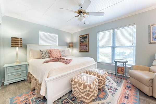A bedroom with a bed, bedside tables, a ceiling fan, a window with blinds, and a patterned rug.