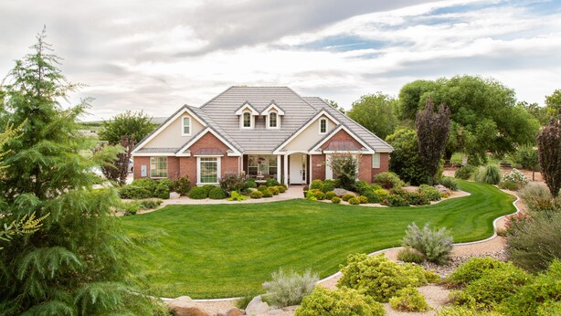 A two-story house with a well-maintained lawn, surrounded by various shrubs and trees.