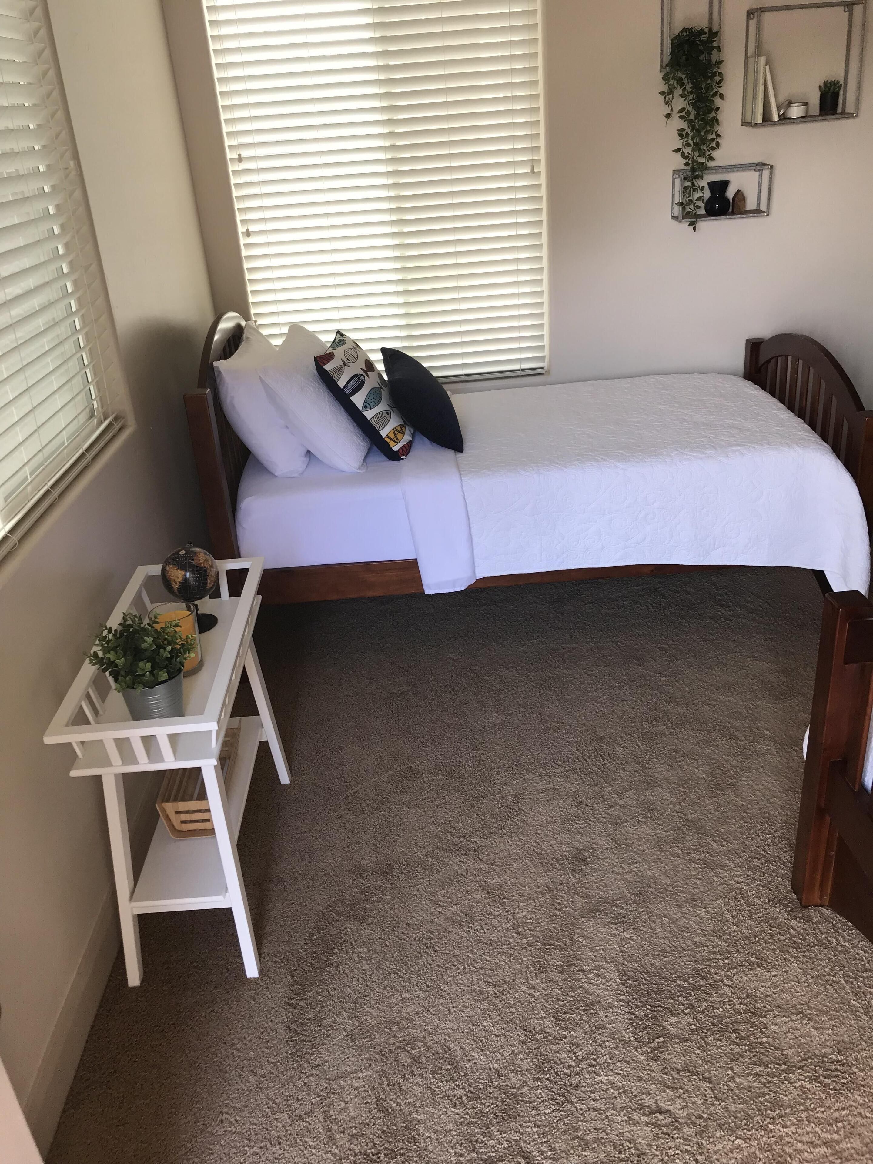 Un dormitorio compacto con una cama individual, un pequeño escritorio blanco y una planta en maceta.