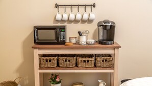 A kitchen area with a microwave, coffee maker, and hanging mugs. There are wicker baskets and a potted plant on the shelves.