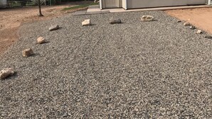 A gravel driveway leading to a building with a door and a satellite dish.