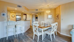 A dining area with a wooden table and white chairs, a kitchen with white cabinets, and a chandelier.