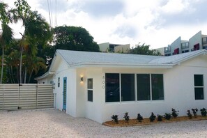 Une maison moderne de plain-pied, avec une façade blanche, un toit en pente et un petit porche à l’avant.