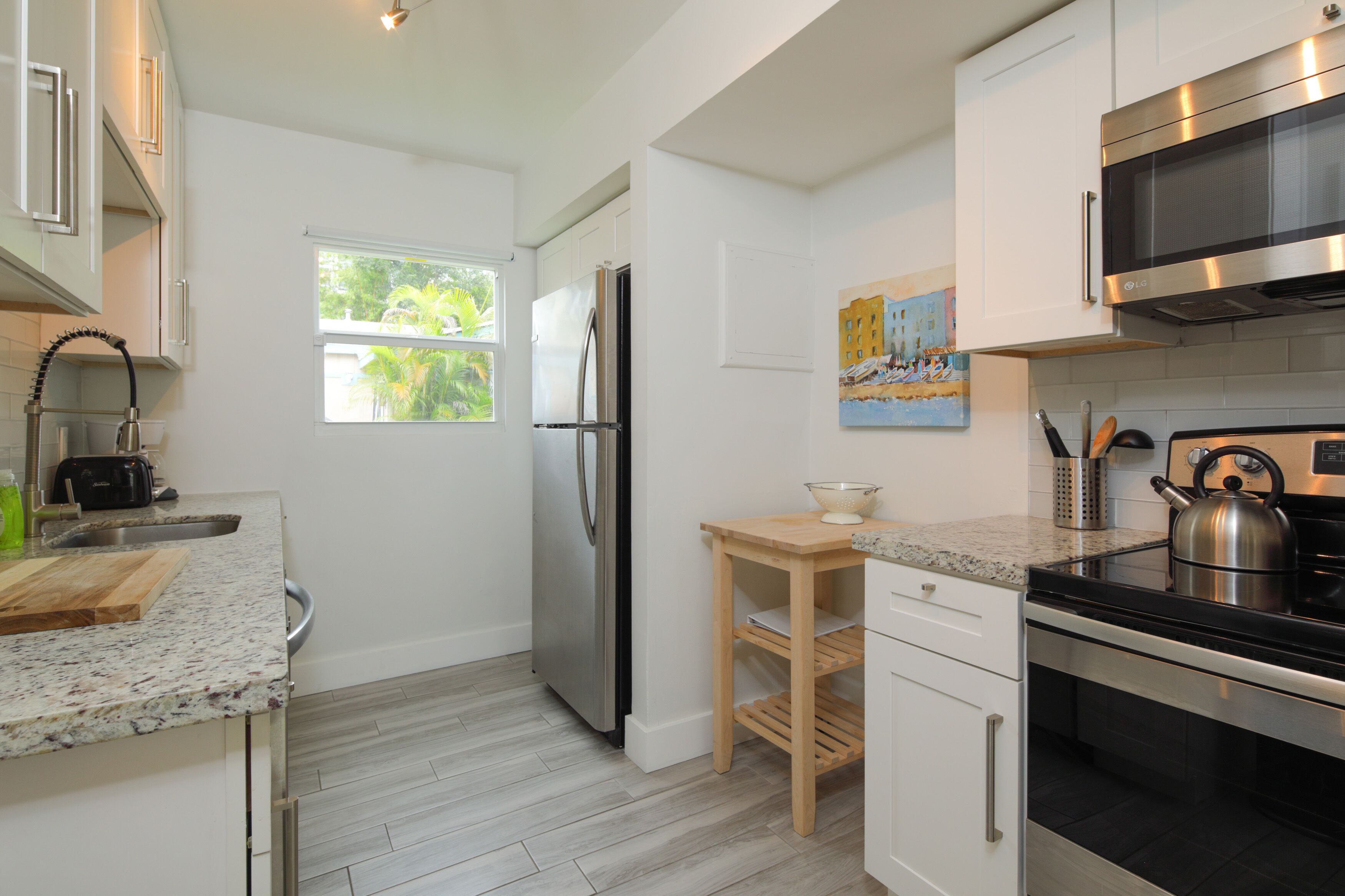 Una cocina moderna con un refrigerador de acero inoxidable, un microondas, un horno, una mesa de madera y un ventanal con vistas a zonas verdes.