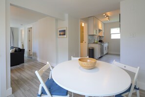 Une cuisine moderne avec des meubles blancs, une table à manger surmontée d’un saladier en bois et une chaise bleue.
