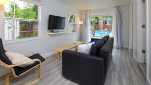 A living room with a black leather sofa, a wooden coffee table, a black chair with a white cushion, a flat-screen TV mounted on the wall, and a view of a swimming pool through glass doors. - Close to beach, downtown, airport. Entire Apt. (Fort Lauderdale)