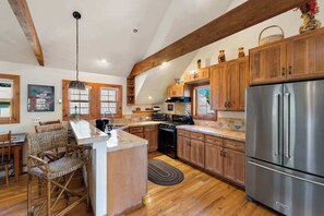 Una cocina con armarios de madera, un refrigerador de acero inoxidable y un comedor con sillas de mimbre.