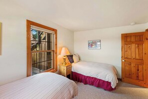 Un dormitorio con dos camas, una ventana, una mesita de noche con lámpara y una puerta.