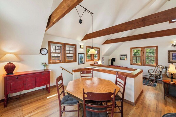 Un comedor con una mesa y sillas de madera, un armario rojo y una isla de cocina con un lavamanos y taburetes.