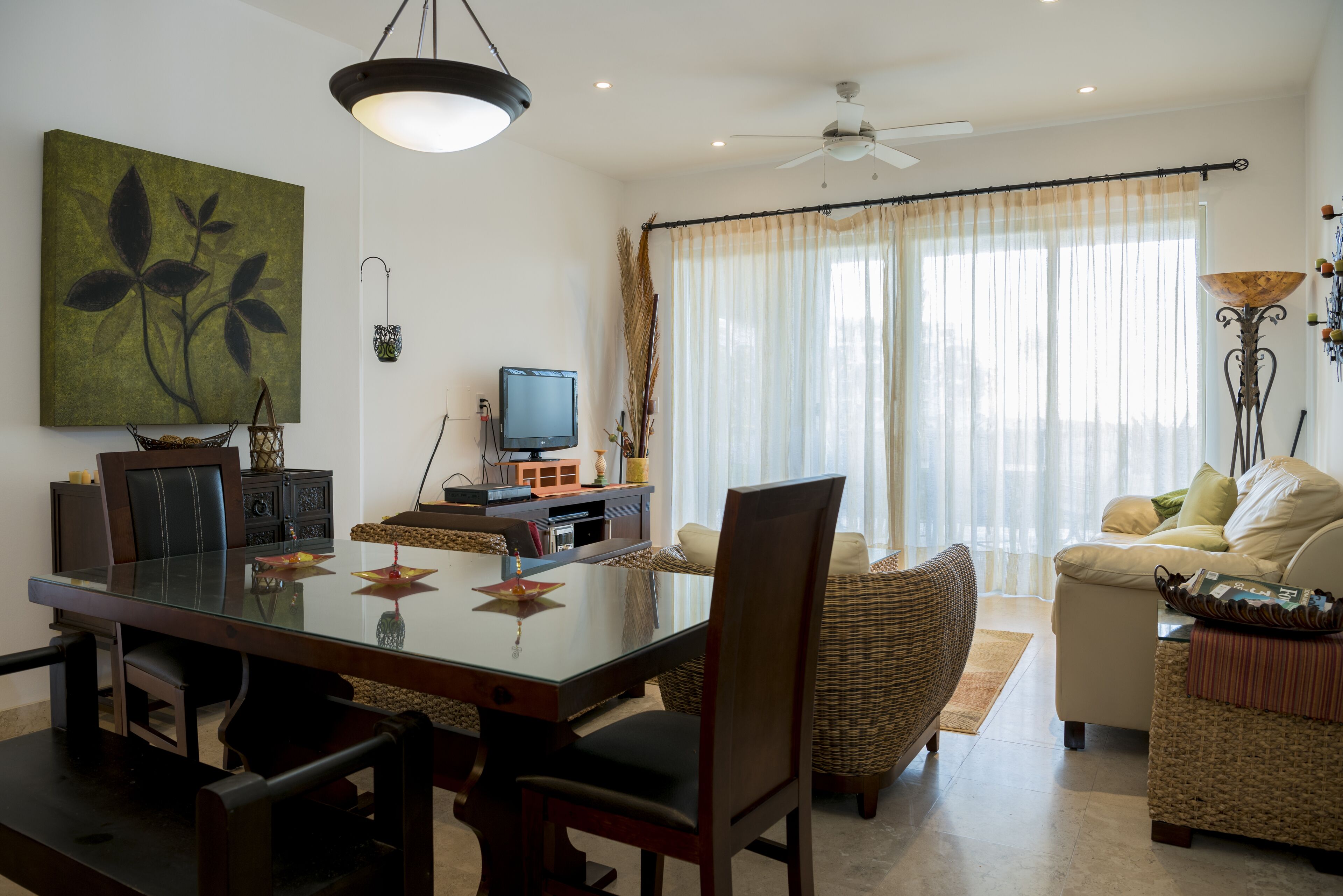 Ein Wohnzimmer mit Esstisch, Stühlen, einer Couch, einem Fernseher und einem Deckenventilator.