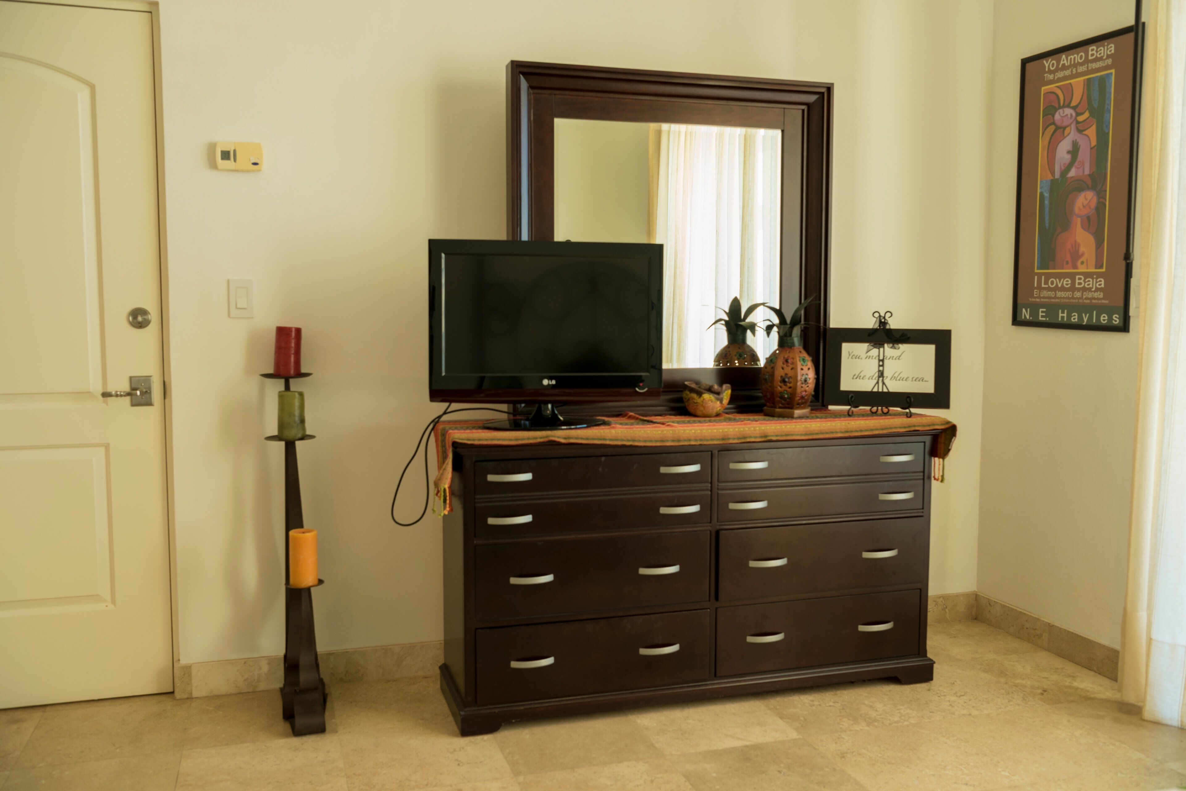 A room with a dark wooden dresser, a flat-screen TV on top, a mirror above the TV, and a framed picture on the wall.