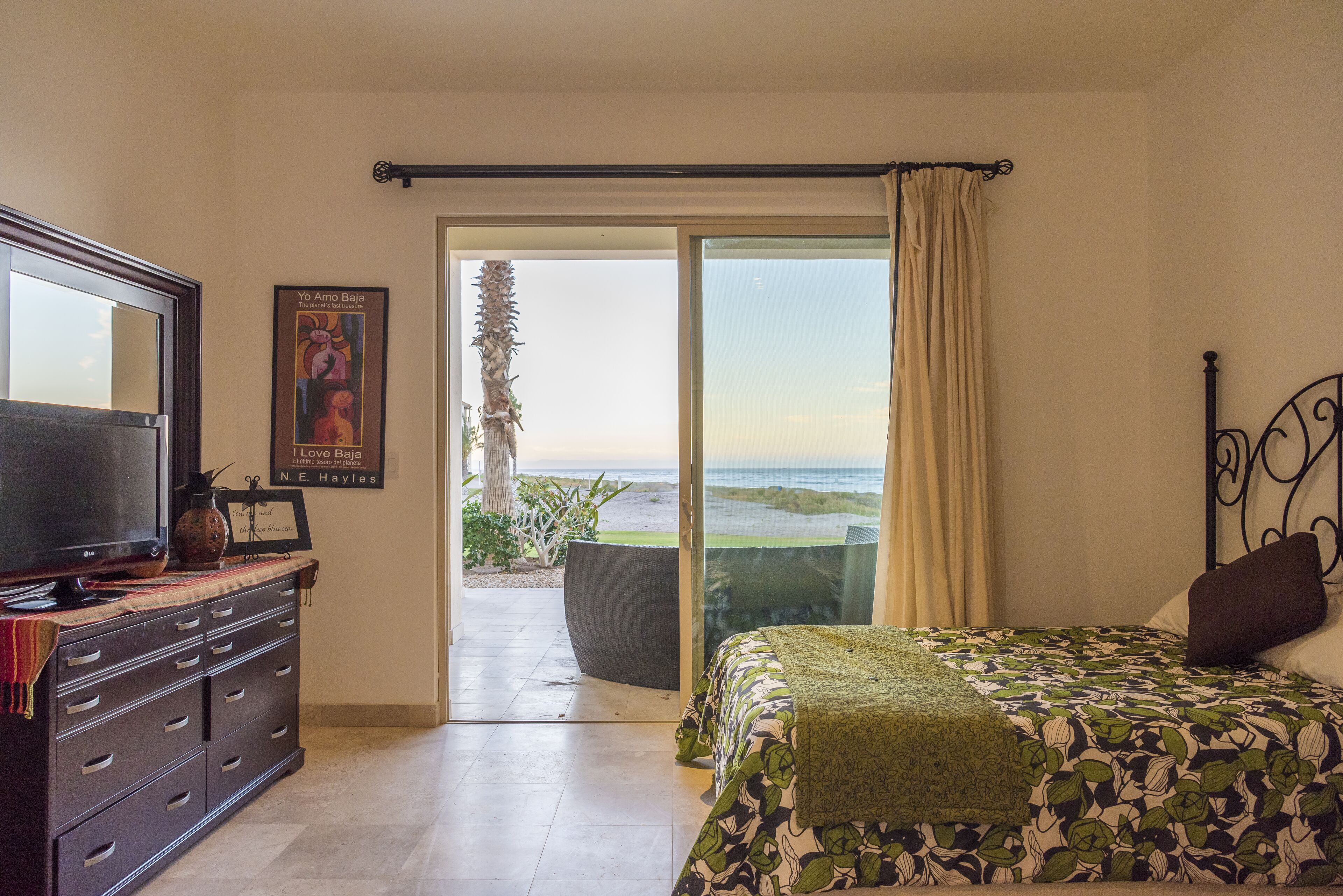 A bedroom with a bed, a TV, a dresser, and a view of the beach.