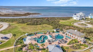 An aerial view of a resort with a large pool, a beach, and a large house.