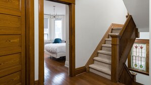 A wooden staircase with a handrail leading to a bedroom with a bed and a window.