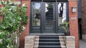 A two-story house with a dark grey roof, a brick facade, and a black front door with a glass panel.