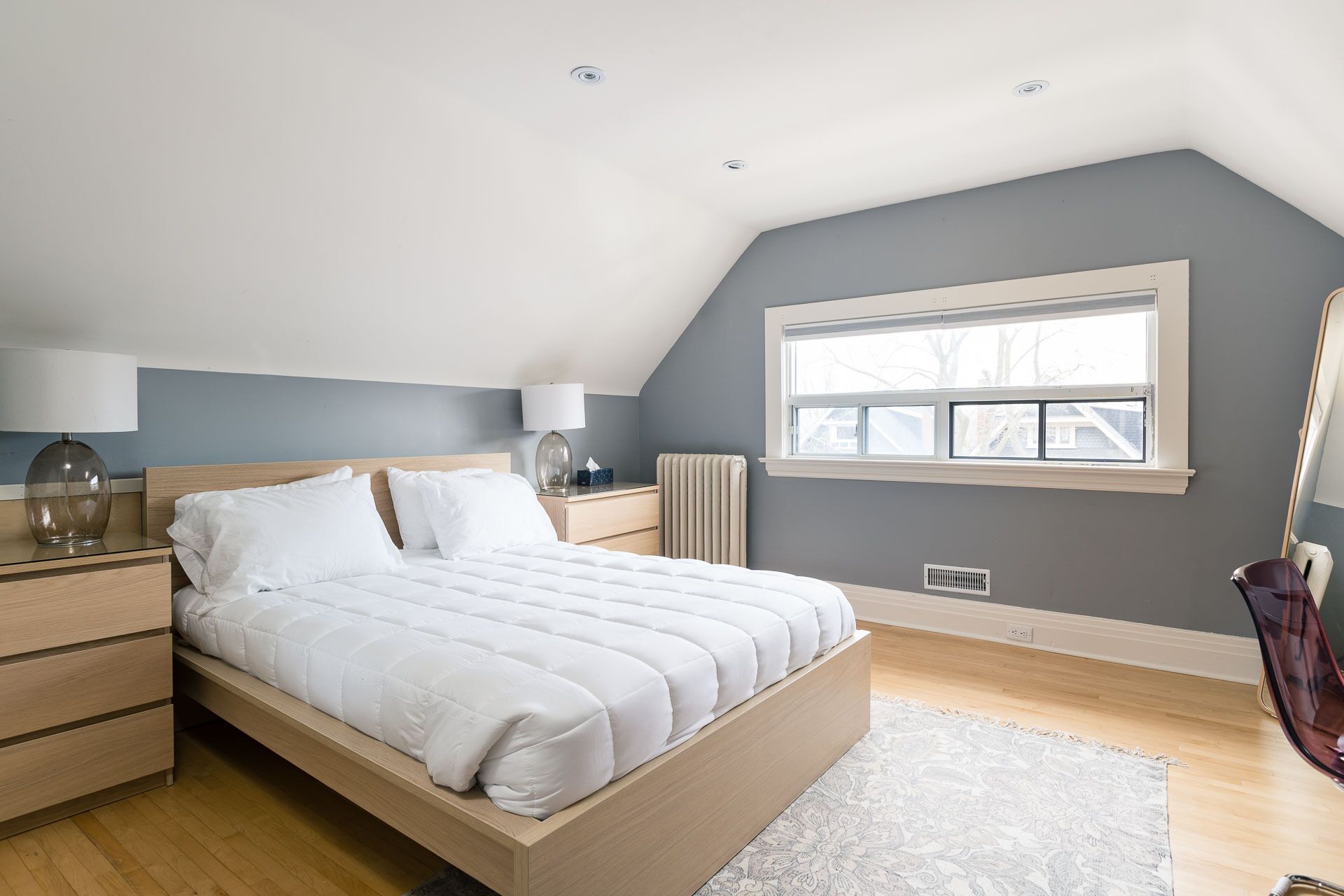A bedroom with a large bed, bedside tables, a window, and a radiator.