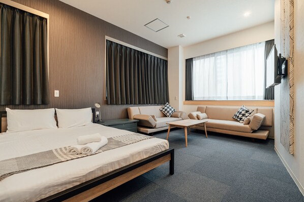 A modern hotel room with a large bed, a sofa, a small table, and a TV mounted on the wall.