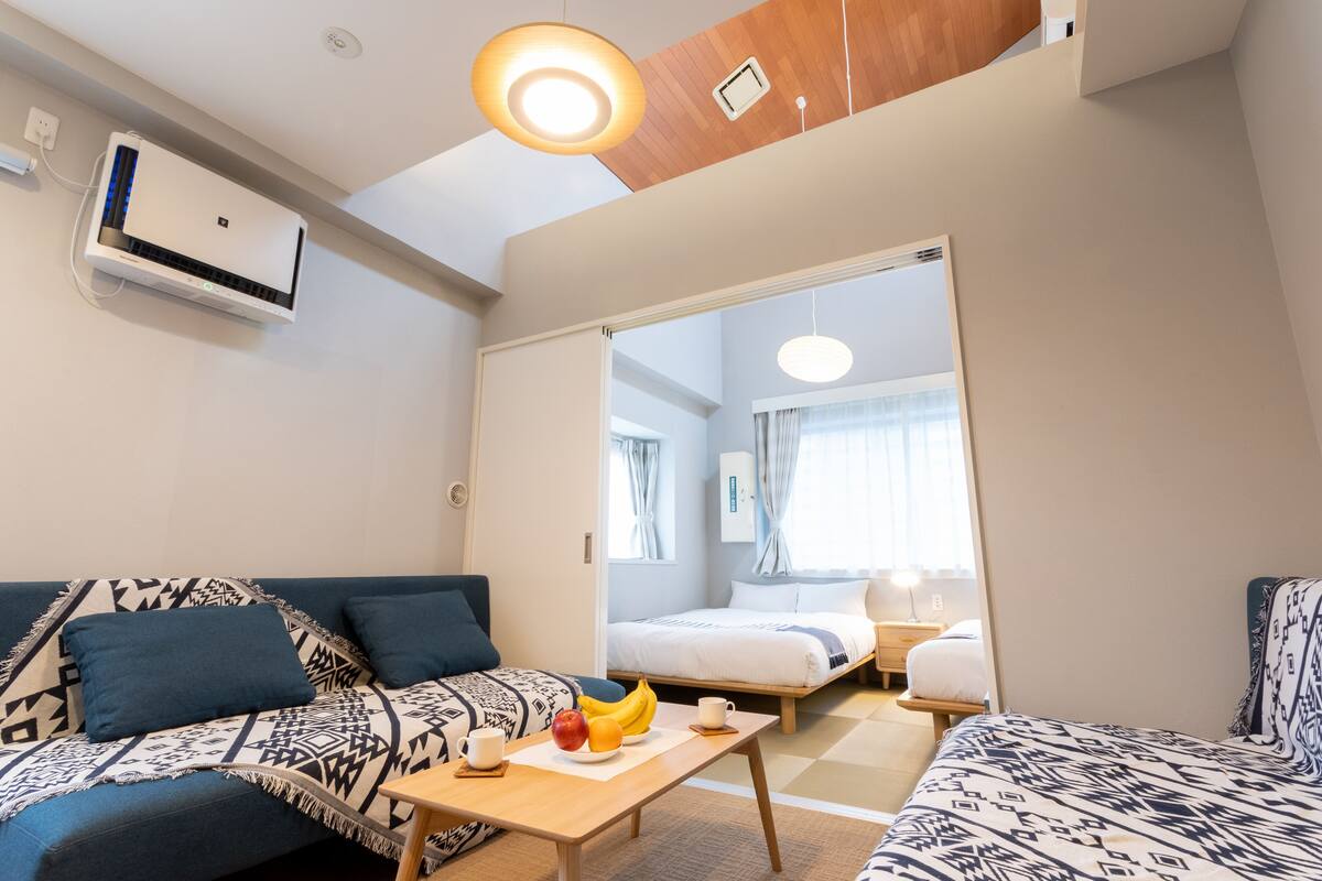 A modern hotel room with a sofa, a small table with fruits, a bed, and a ceiling fan.