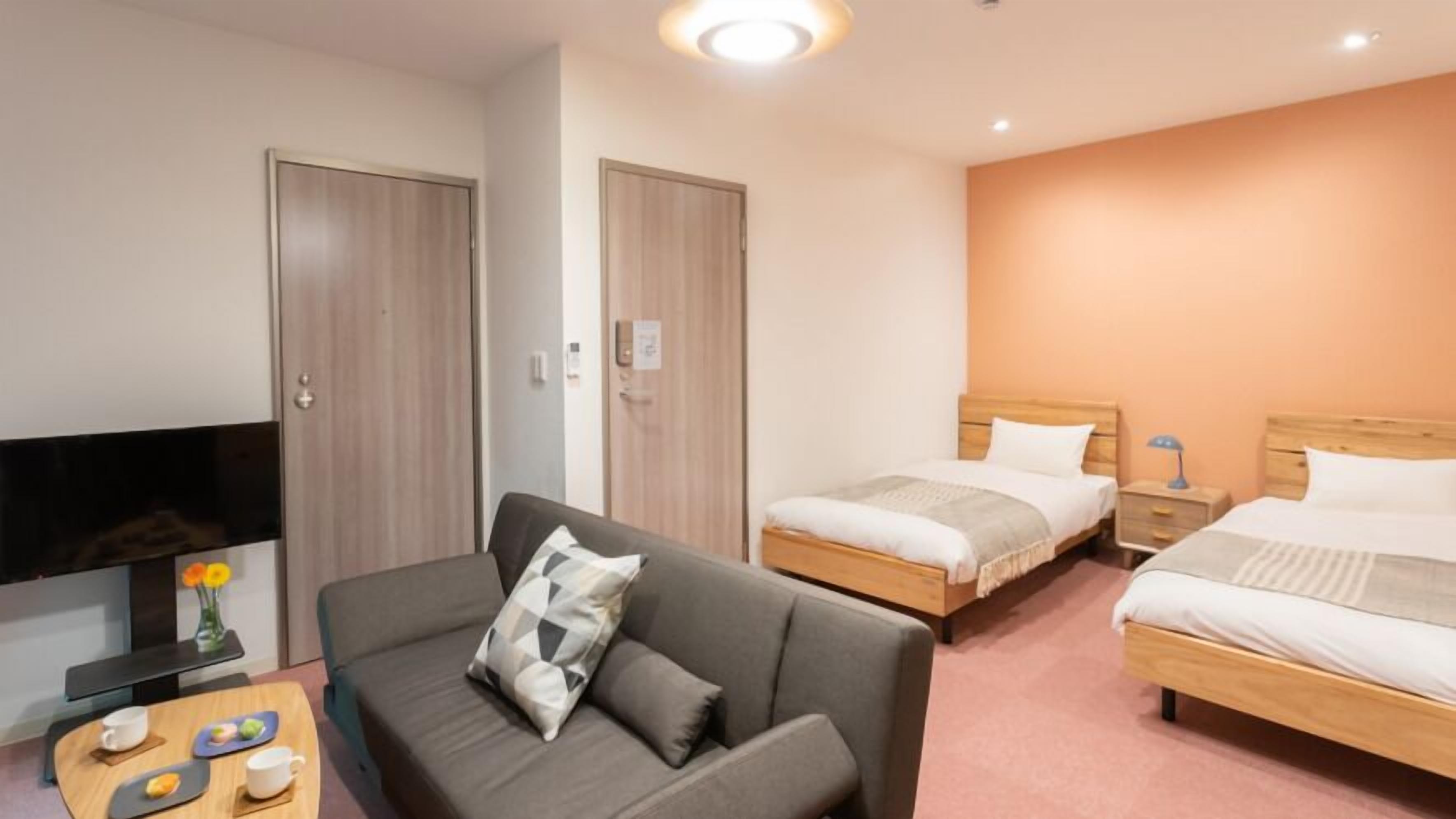 Habitació d'hotel amb sofà, dos llits individuals, televisió i una taula petita amb tasses i un ram.