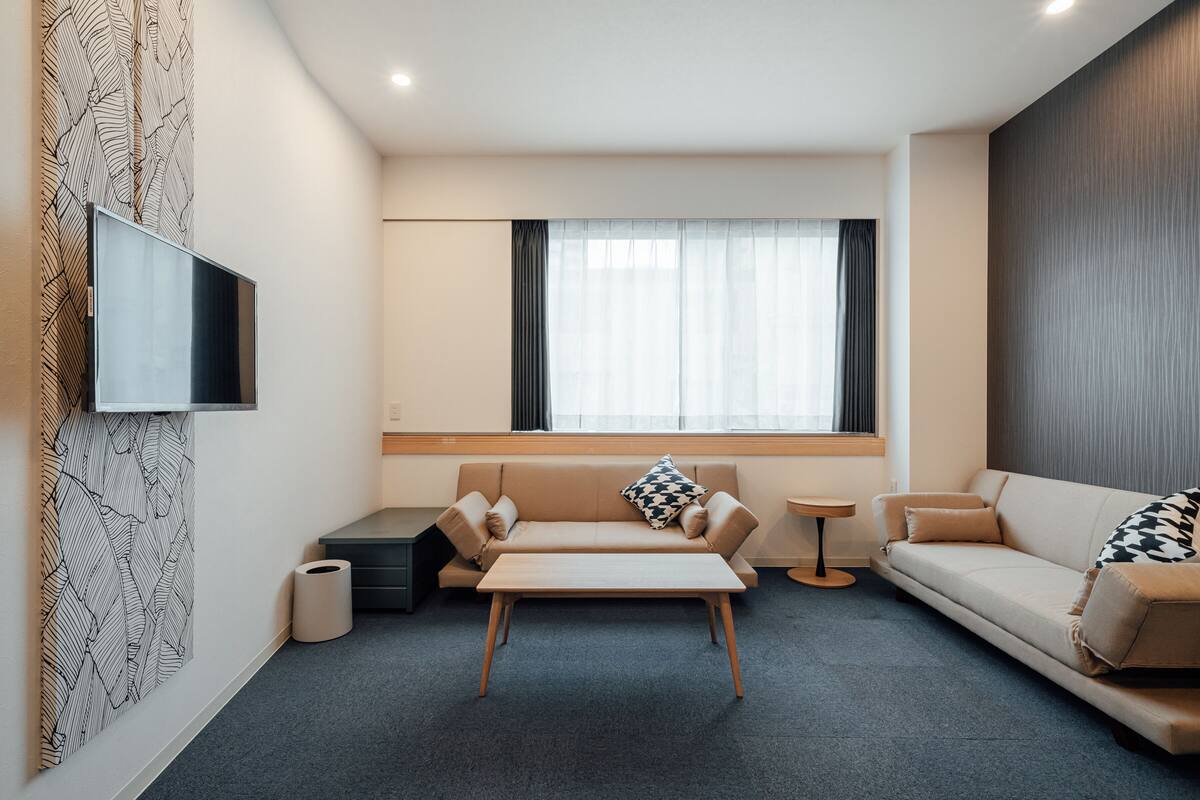 A modern living room with a sofa, a coffee table, a TV mounted on the wall, and a window with curtains.
