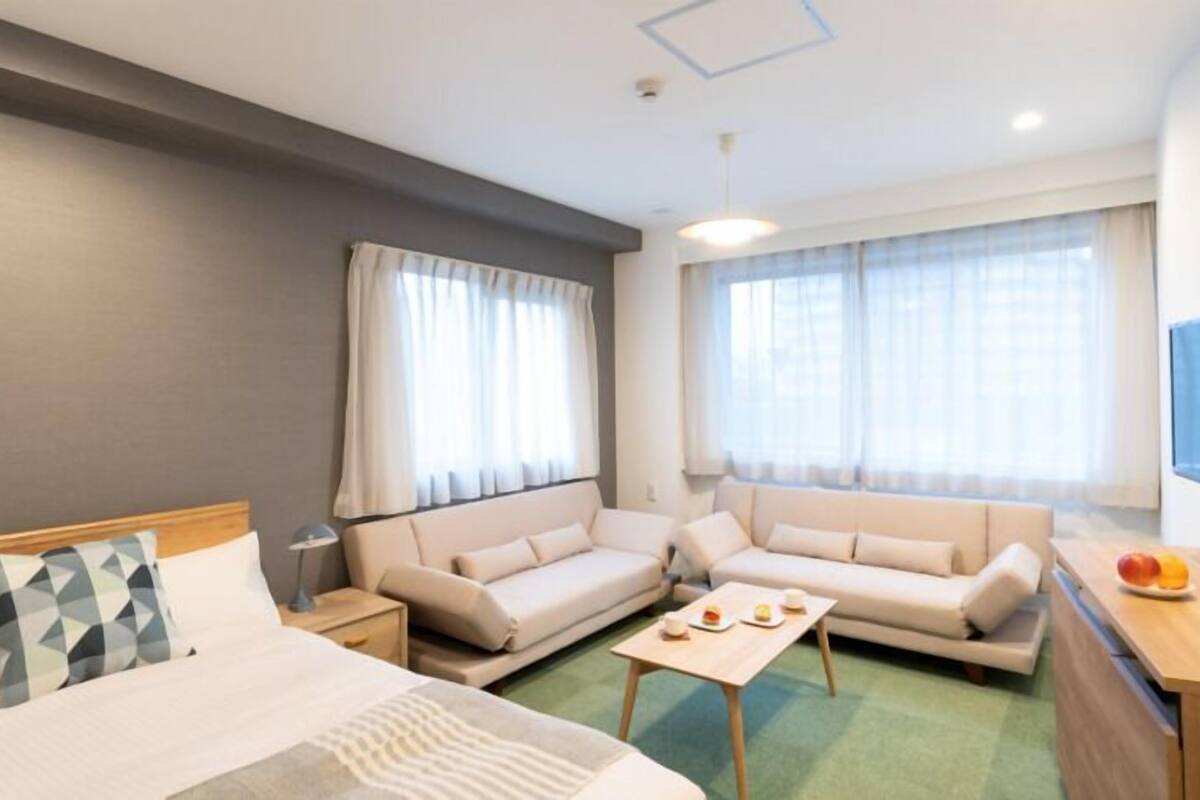 A hotel room with a bed, two sofas, a small table, a TV, and a window with curtains.