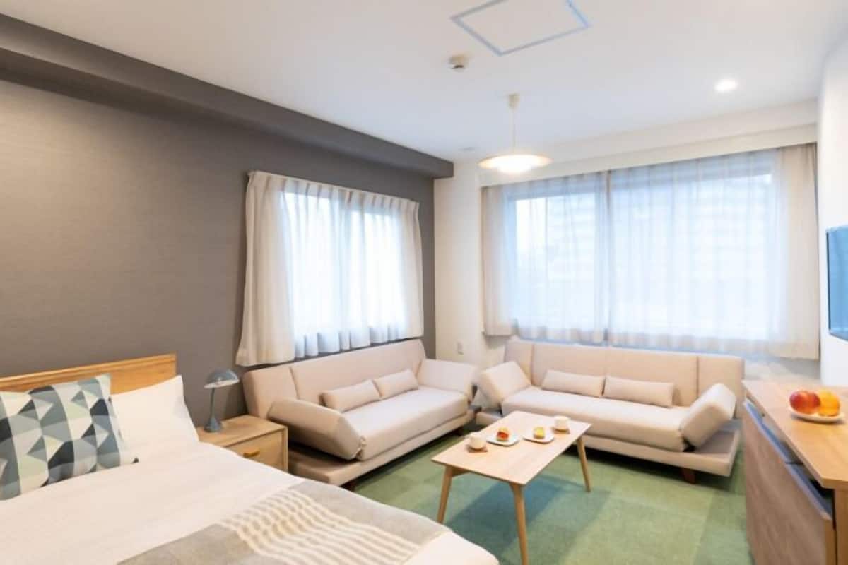 Hotellihuone, jossa on sänky, kaksi sohvaa, pieni pöytä, televisio ja ikkuna, jossa on verhot.