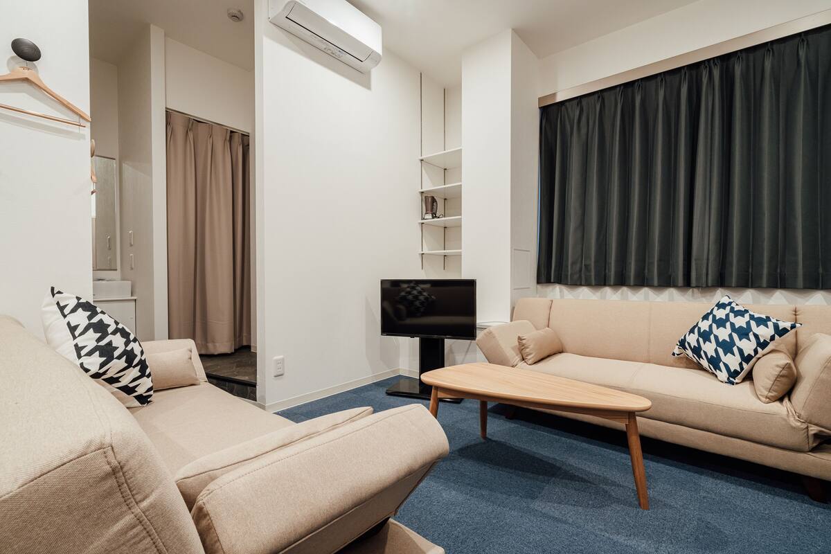 A modern living room with a beige sofa, a wooden coffee table, and a TV on a stand.